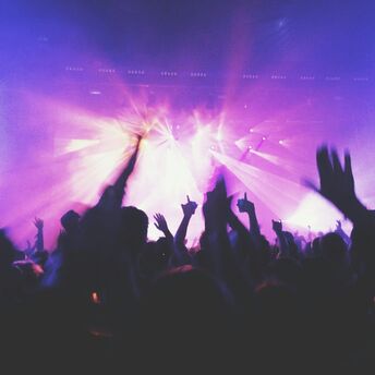 A vibrant crowd dancing under purple and blue stage lights at a music festival