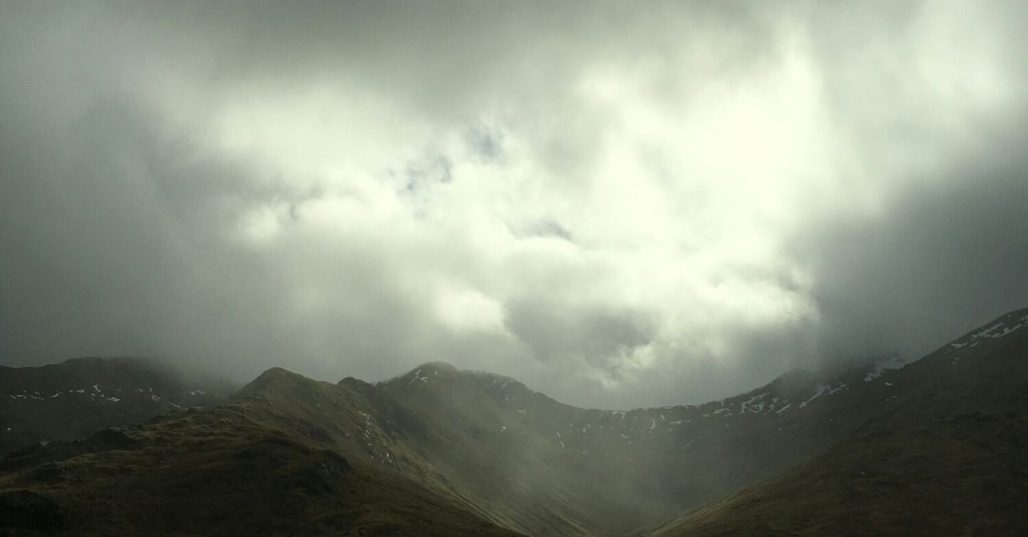 Dark storm clouds over a mountain valley with misty light breaking through