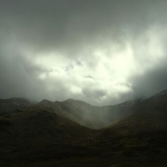 Dark storm clouds over a mountain valley with misty light breaking through