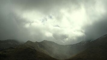 Dark storm clouds over a mountain valley with misty light breaking through