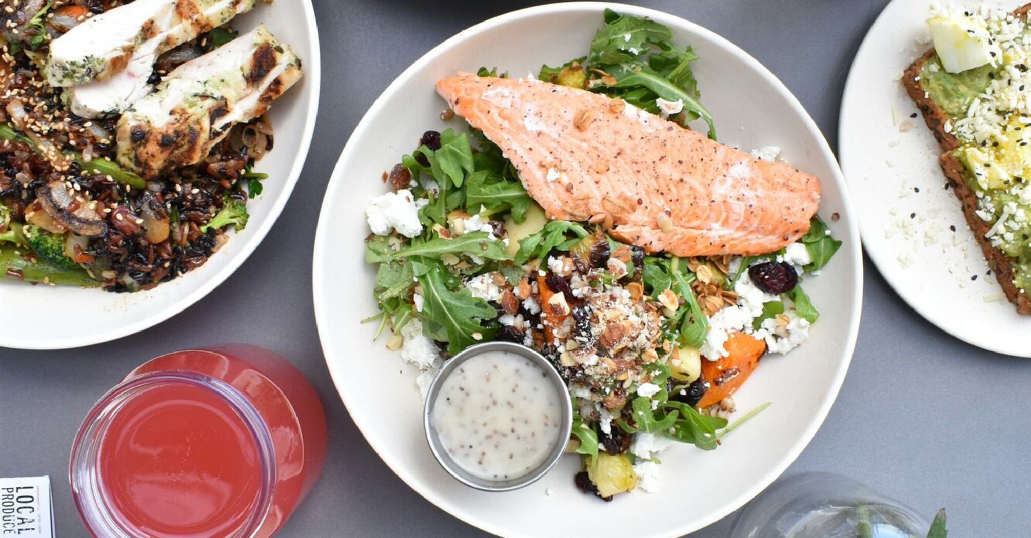 A variety of fresh and colorful gourmet dishes, including grilled salmon salad, roasted vegetables, hummus with flatbread, and refreshing beverages on a table