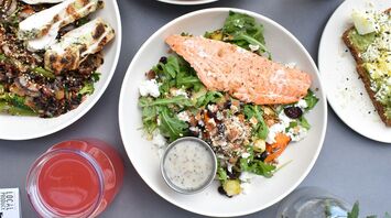 A variety of fresh and colorful gourmet dishes, including grilled salmon salad, roasted vegetables, hummus with flatbread, and refreshing beverages on a table