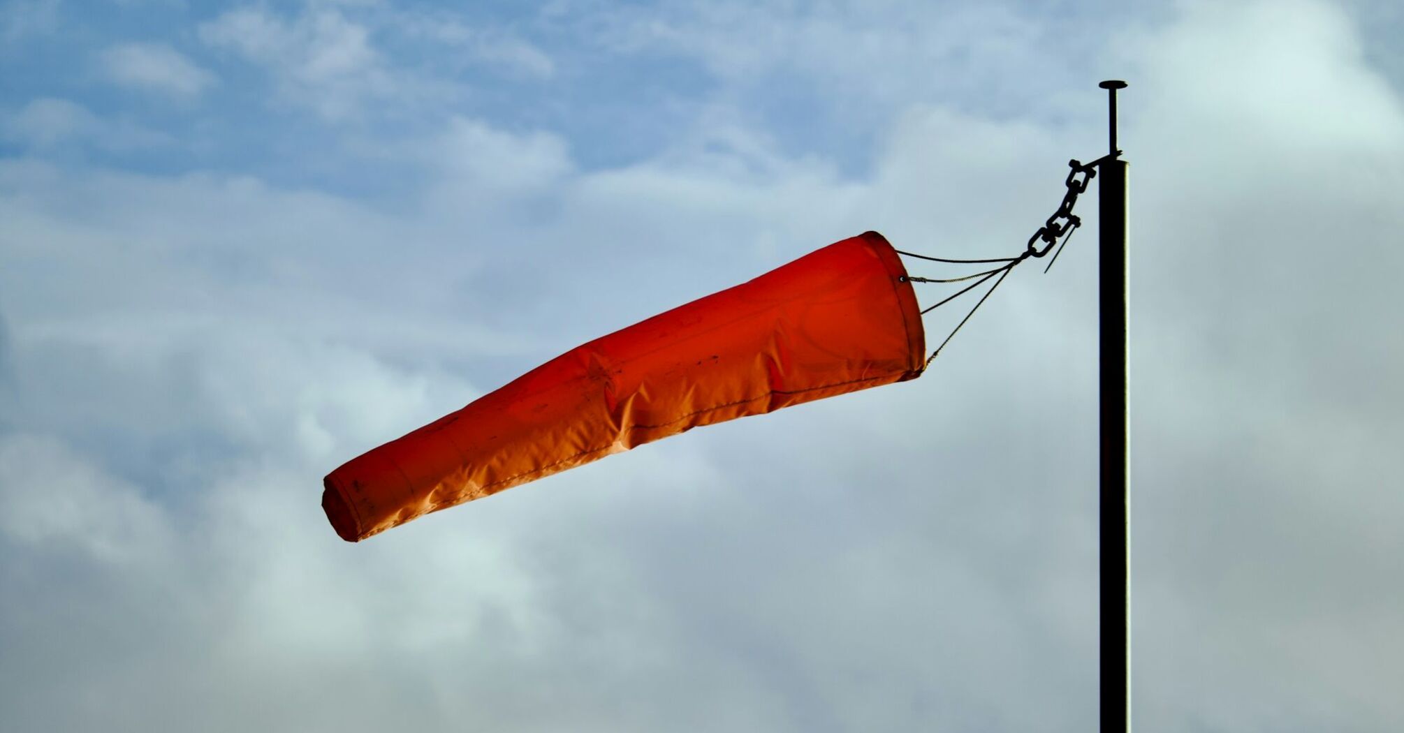 Orange windsock blowing in strong winds against a cloudy sky