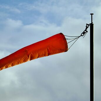 Orange windsock blowing in strong winds against a cloudy sky