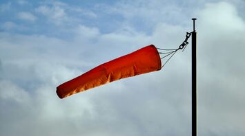 Orange windsock blowing in strong winds against a cloudy sky