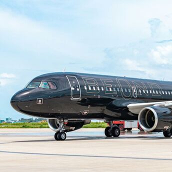 A beOnd luxury aircraft with a sleek black exterior parked on the runway under a blue sky