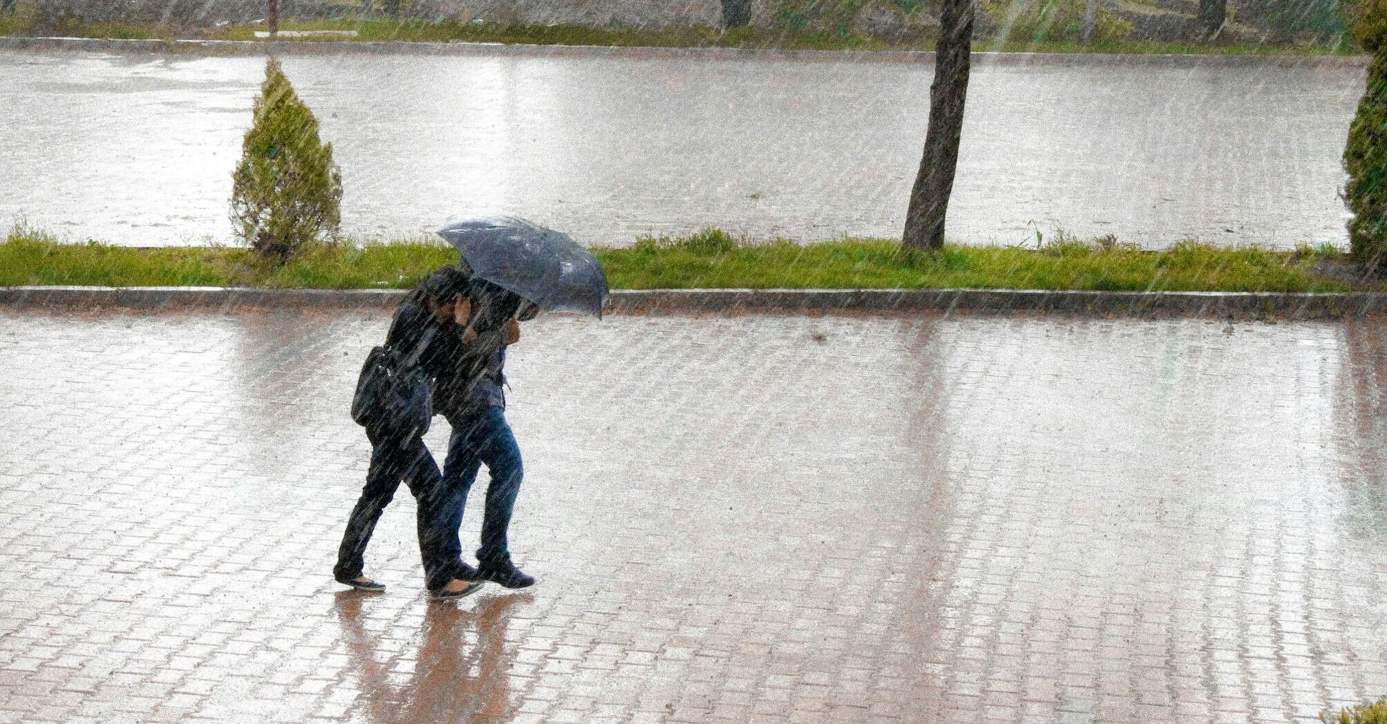 Two people walking under an umbrella during heavy rain on a flooded pavement