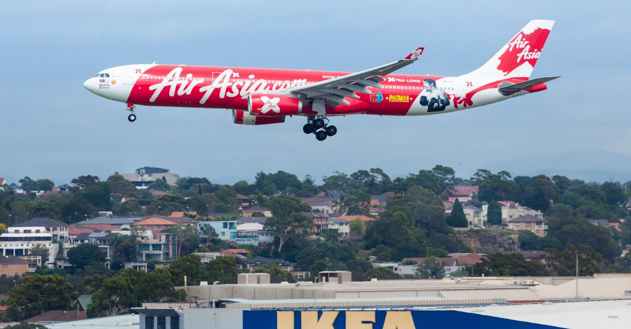 AirAsia X Airbus A330 approaching landing with a promotional livery, flying over an IKEA store and residential area