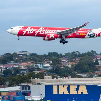 AirAsia X Airbus A330 approaching landing with a promotional livery, flying over an IKEA store and residential area