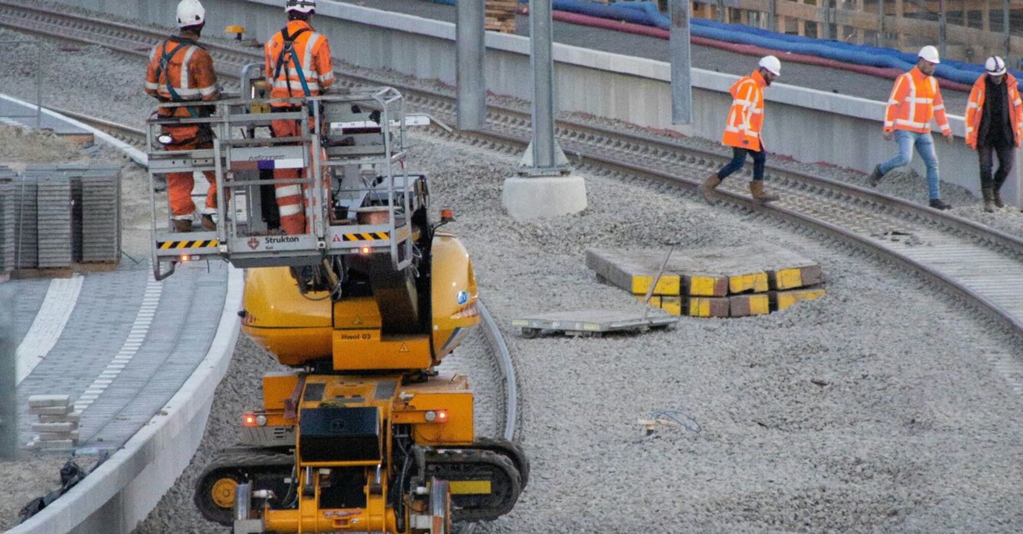 Railway construction workers in high-visibility clothing working on track upgrades with heavy machinery