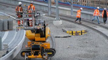 Railway construction workers in high-visibility clothing working on track upgrades with heavy machinery