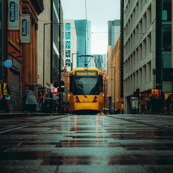 A yellow Manchester tram traveling through a wet city street with modern and historic buildings in the background