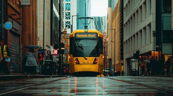 A yellow Manchester tram traveling through a wet city street with modern and historic buildings in the background