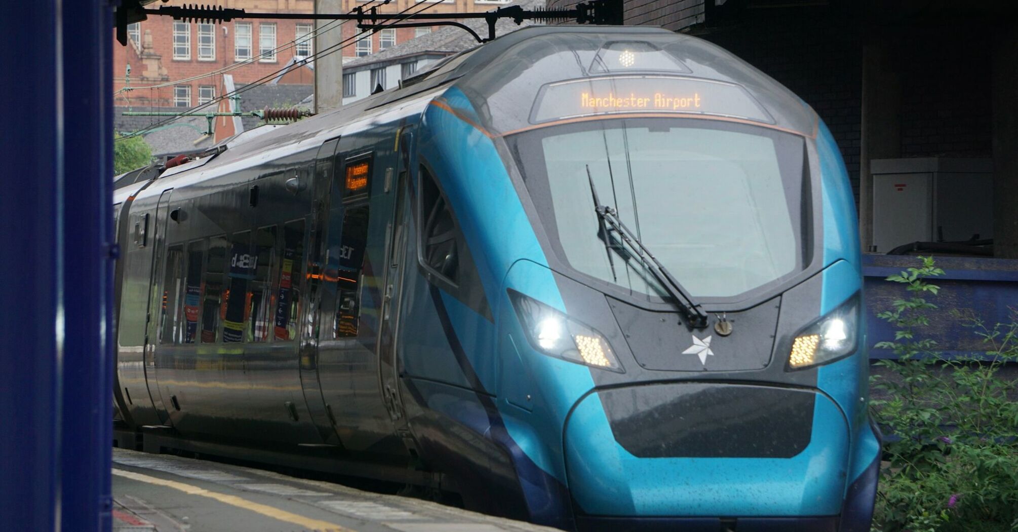 A modern TransPennine Express train at a station platform, displaying its destination as Manchester Airport