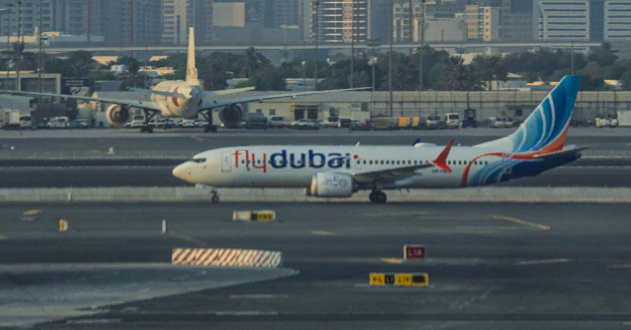 A flydubai aircraft taxiing at Dubai International Airport with the city's skyline in the background