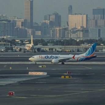 A flydubai aircraft taxiing at Dubai International Airport with the city's skyline in the background