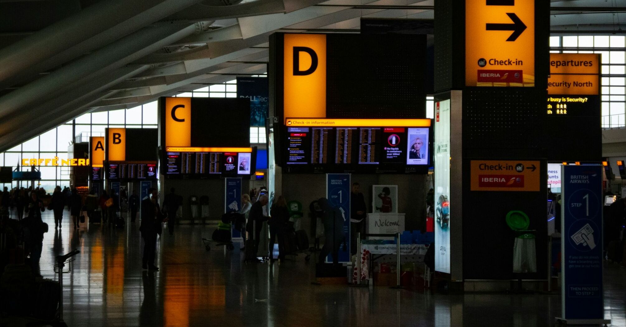 Busy check-in area at Heathrow Airport with illuminated signs for gates A to E