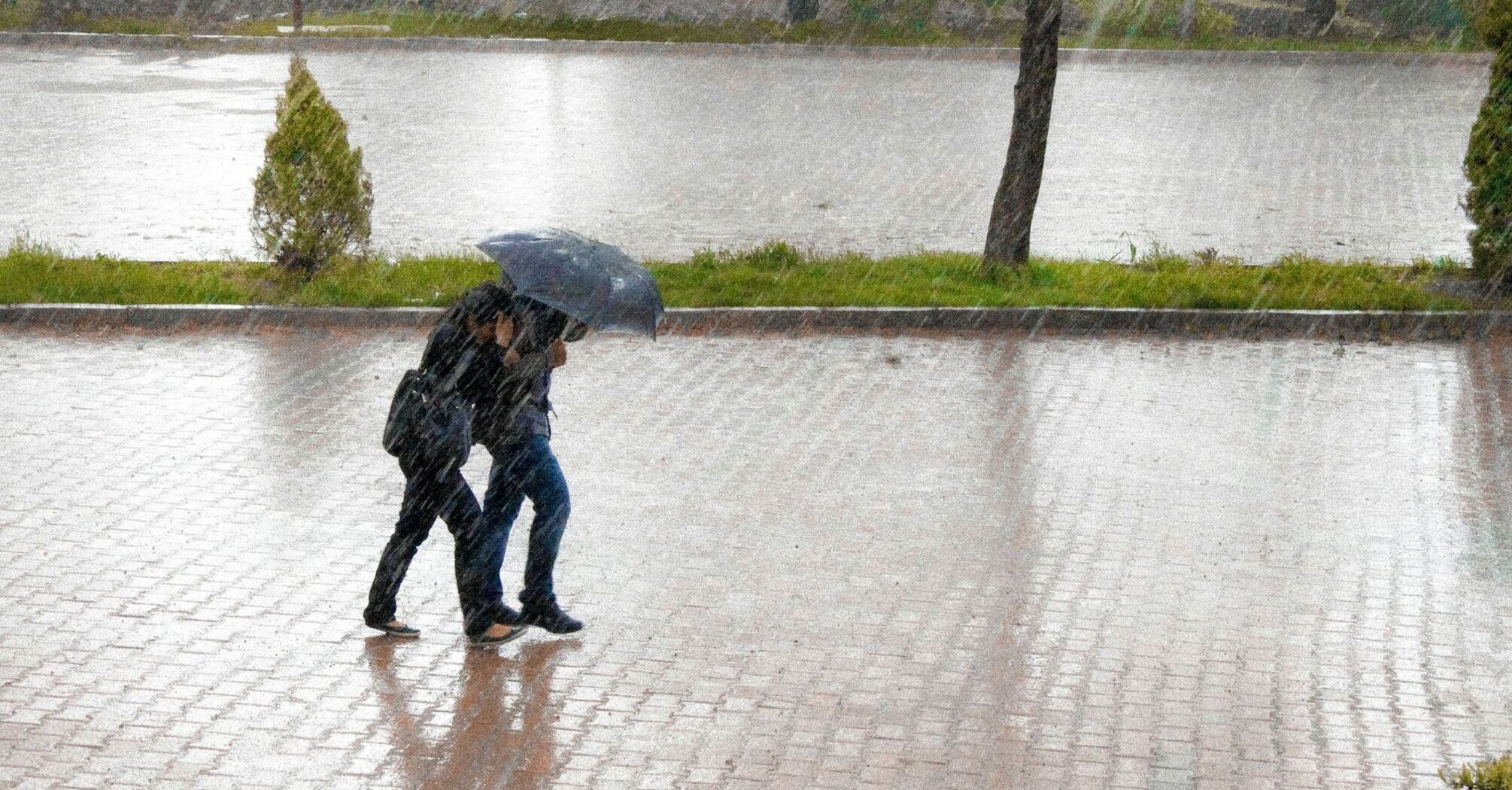 Two people walking under an umbrella during heavy rain on a wet pavement