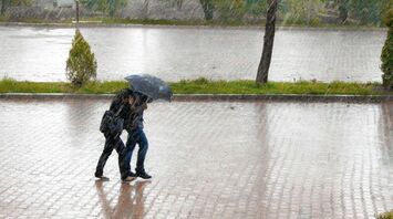 Two people walking under an umbrella during heavy rain on a wet pavement