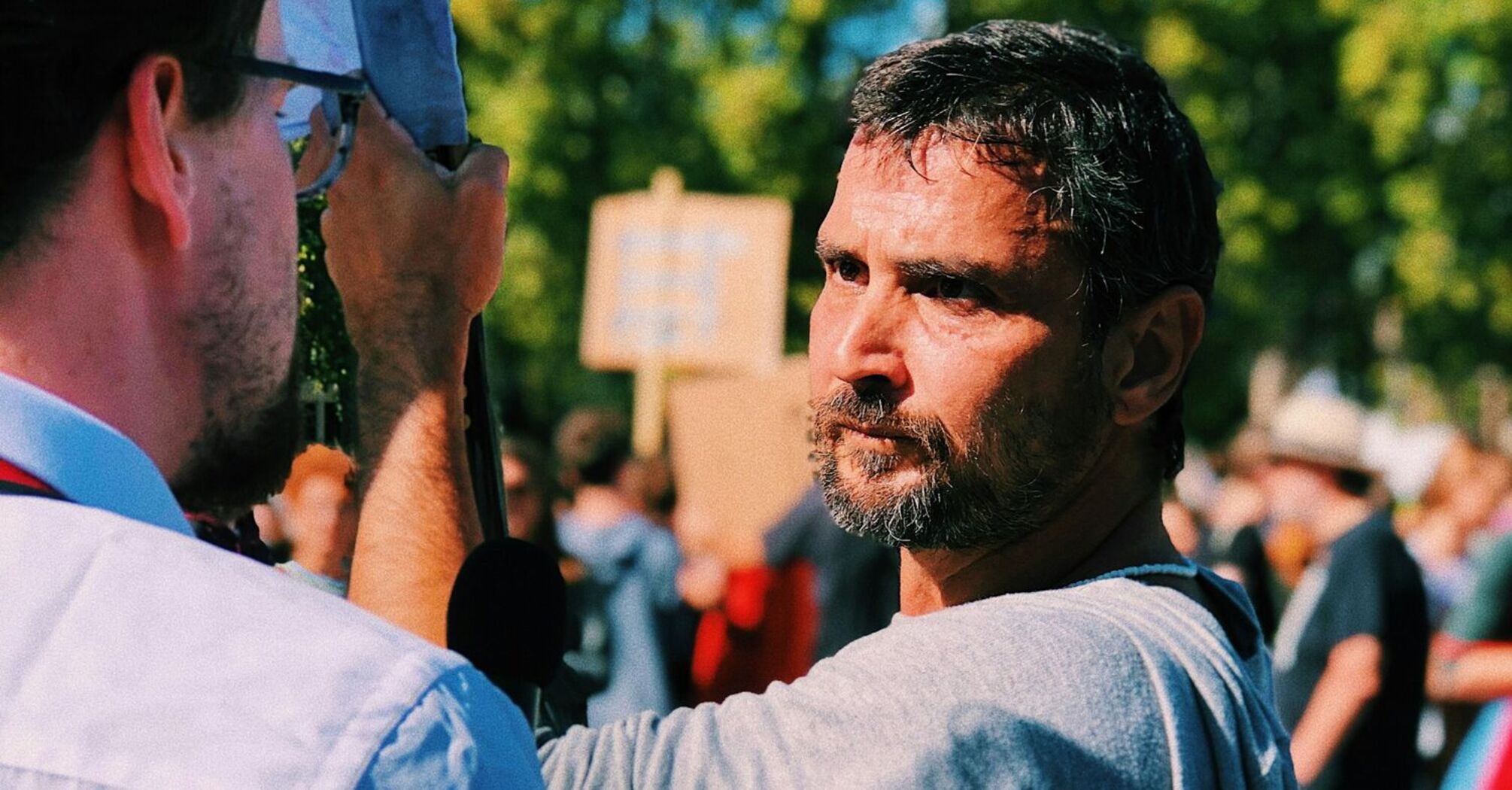 A man at a public demonstration holding a sign, engaged in a serious conversation with another protester