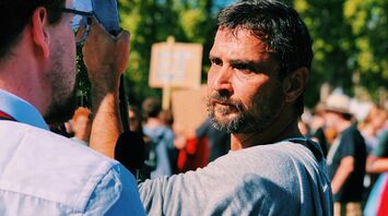 A man at a public demonstration holding a sign, engaged in a serious conversation with another protester