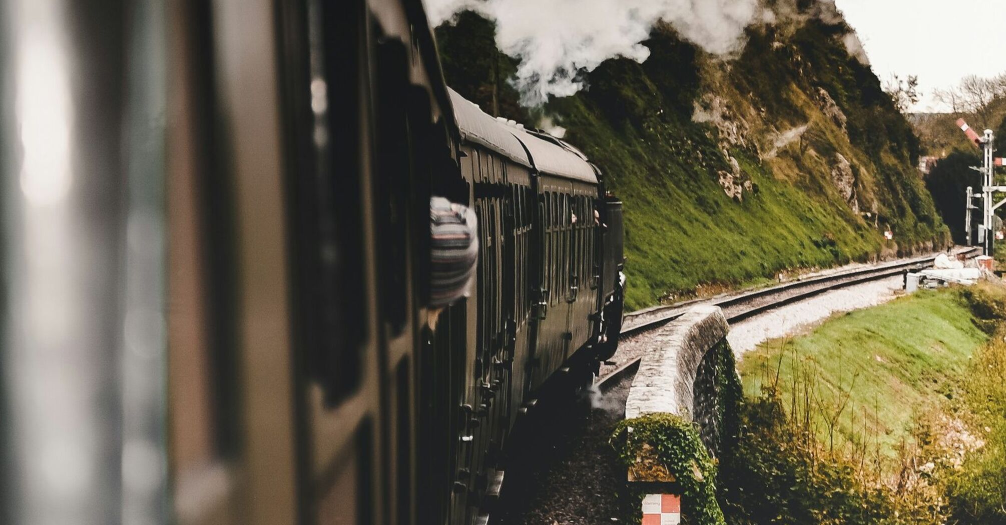 Vintage steam train traveling through a scenic countryside with smoke billowing from its engine