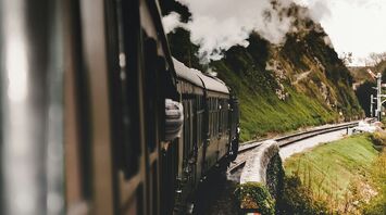 Vintage steam train traveling through a scenic countryside with smoke billowing from its engine