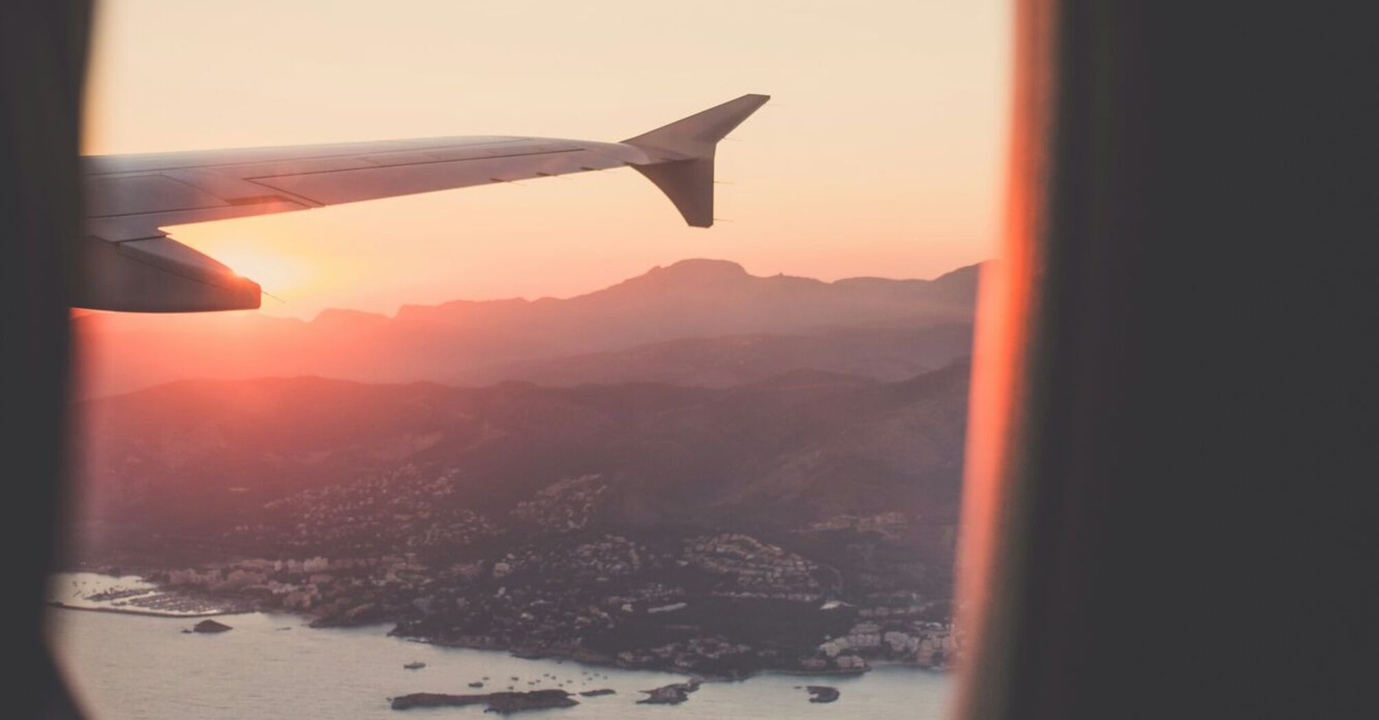 View from an airplane window showing a scenic coastline and mountains at sunset