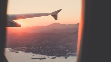 View from an airplane window showing a scenic coastline and mountains at sunset