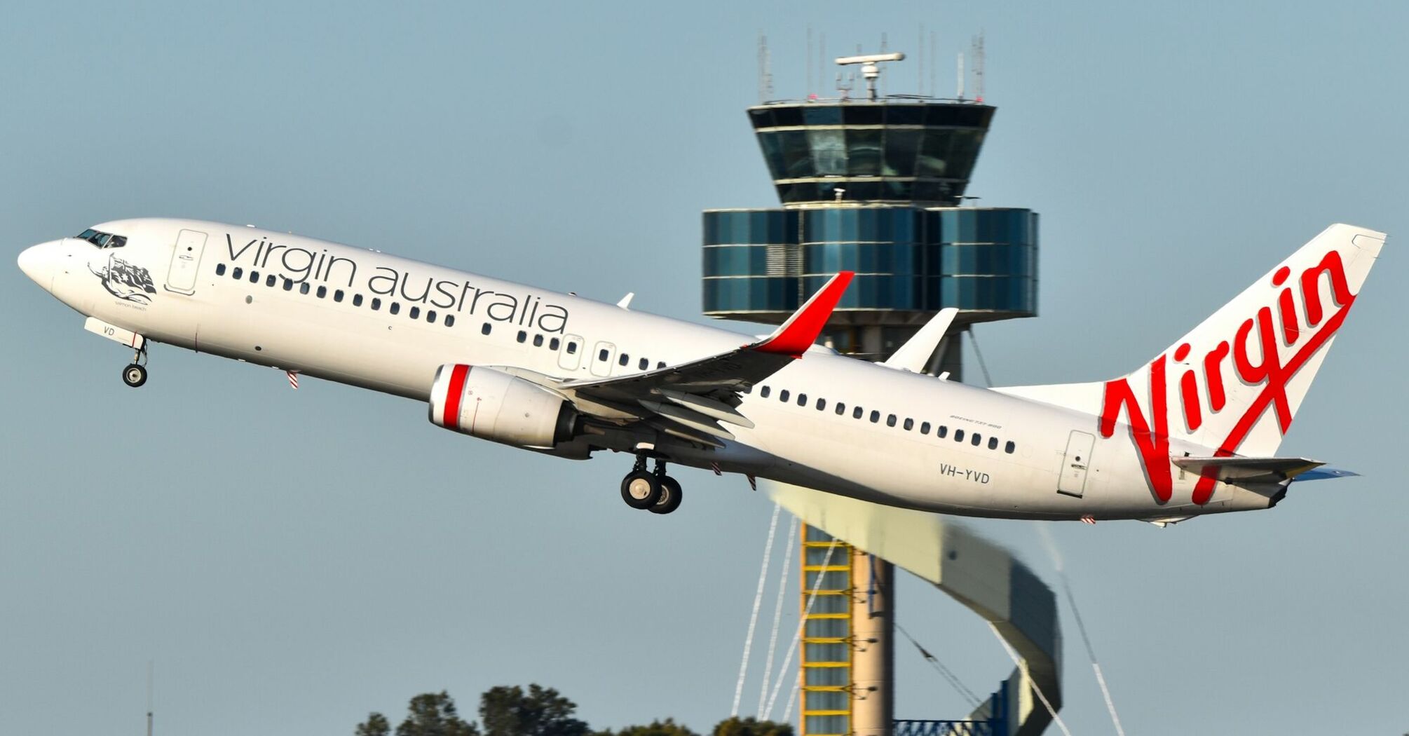 Virgin Australia plane taking off with an air traffic control tower in the background