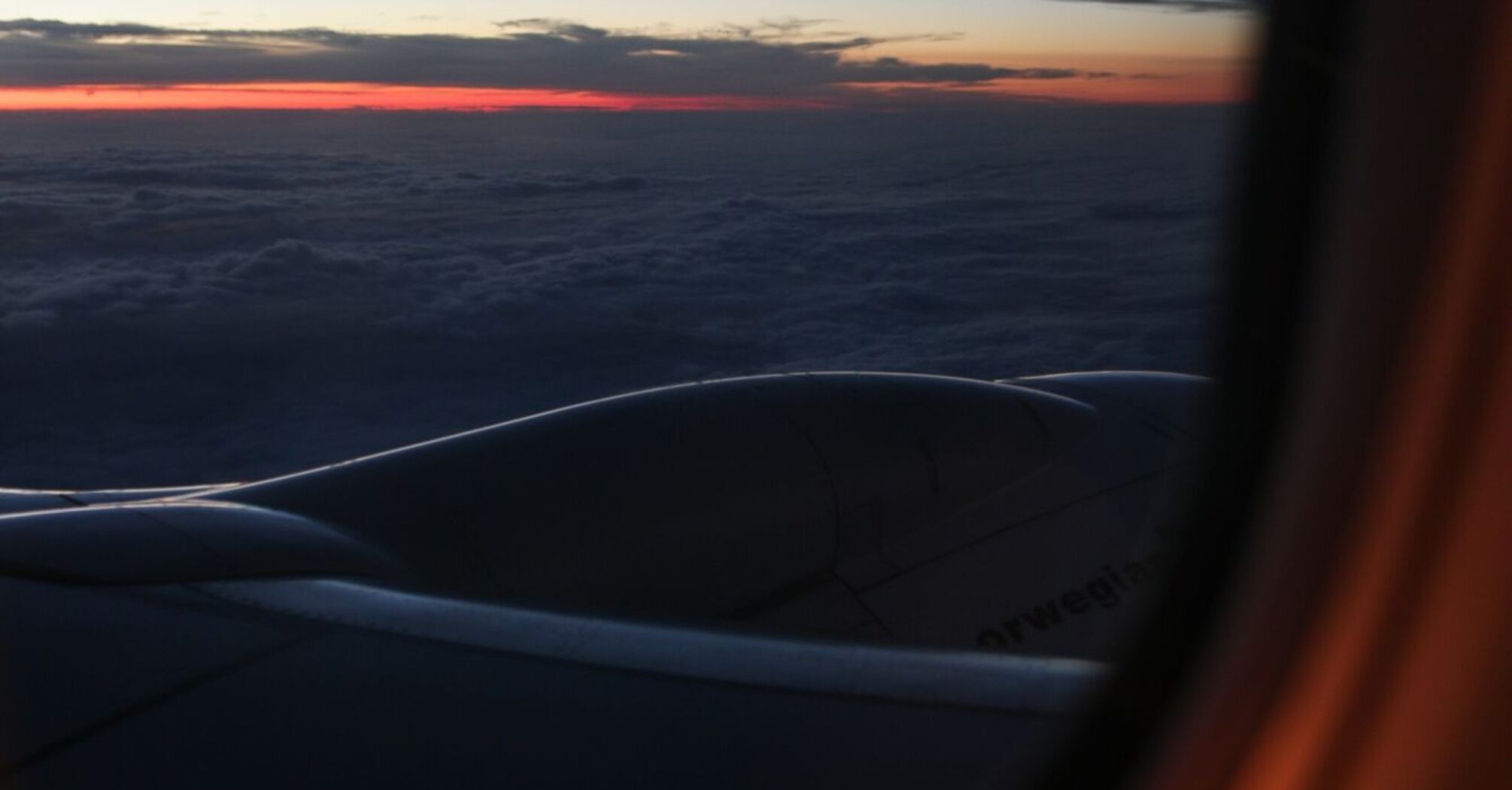 View from an airplane window at sunset, showing clouds, a Norwegian aircraft engine, and a colorful sky