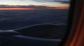 View from an airplane window at sunset, showing clouds, a Norwegian aircraft engine, and a colorful sky