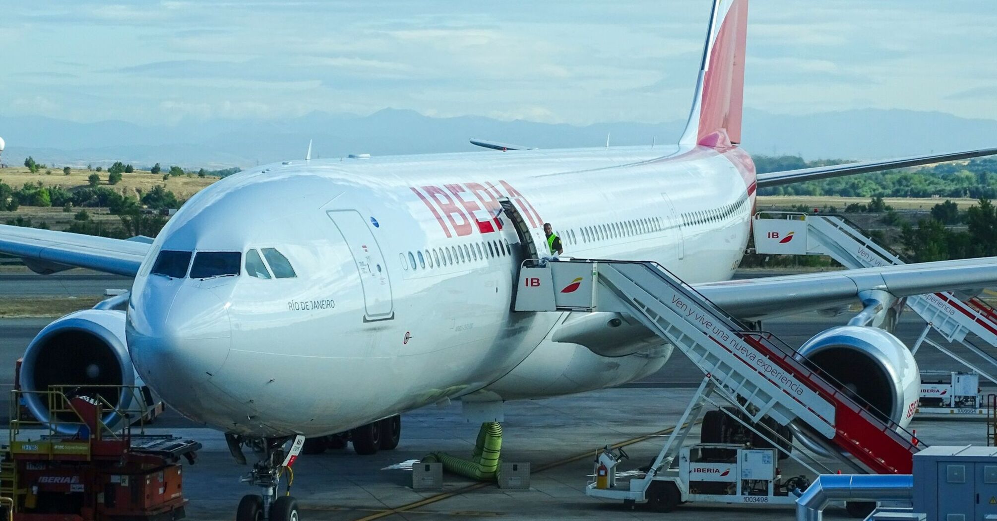 Iberia aircraft parked at the airport gate with boarding stairs and ground staff preparing for departure