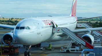 Iberia aircraft parked at the airport gate with boarding stairs and ground staff preparing for departure