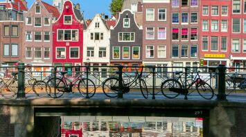 Bicycles parked on a bridge over a canal in Amsterdam with colorful historic buildings in the background
