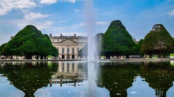 A scenic view of Hampton Court Palace's gardens with a fountain reflecting in the water