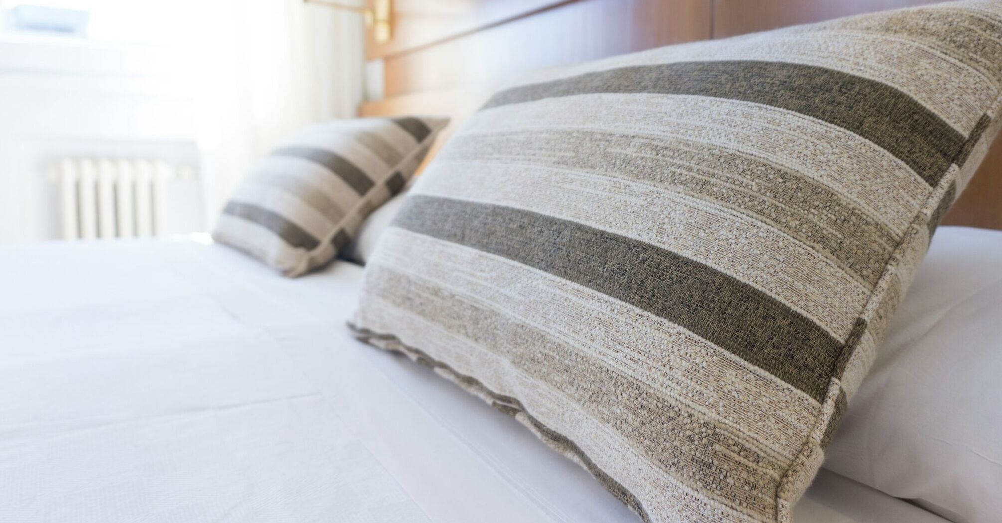 Close-up of striped pillows on a neatly made hotel bed with a wooden headboard in a bright room