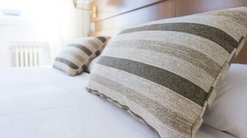Close-up of striped pillows on a neatly made hotel bed with a wooden headboard in a bright room
