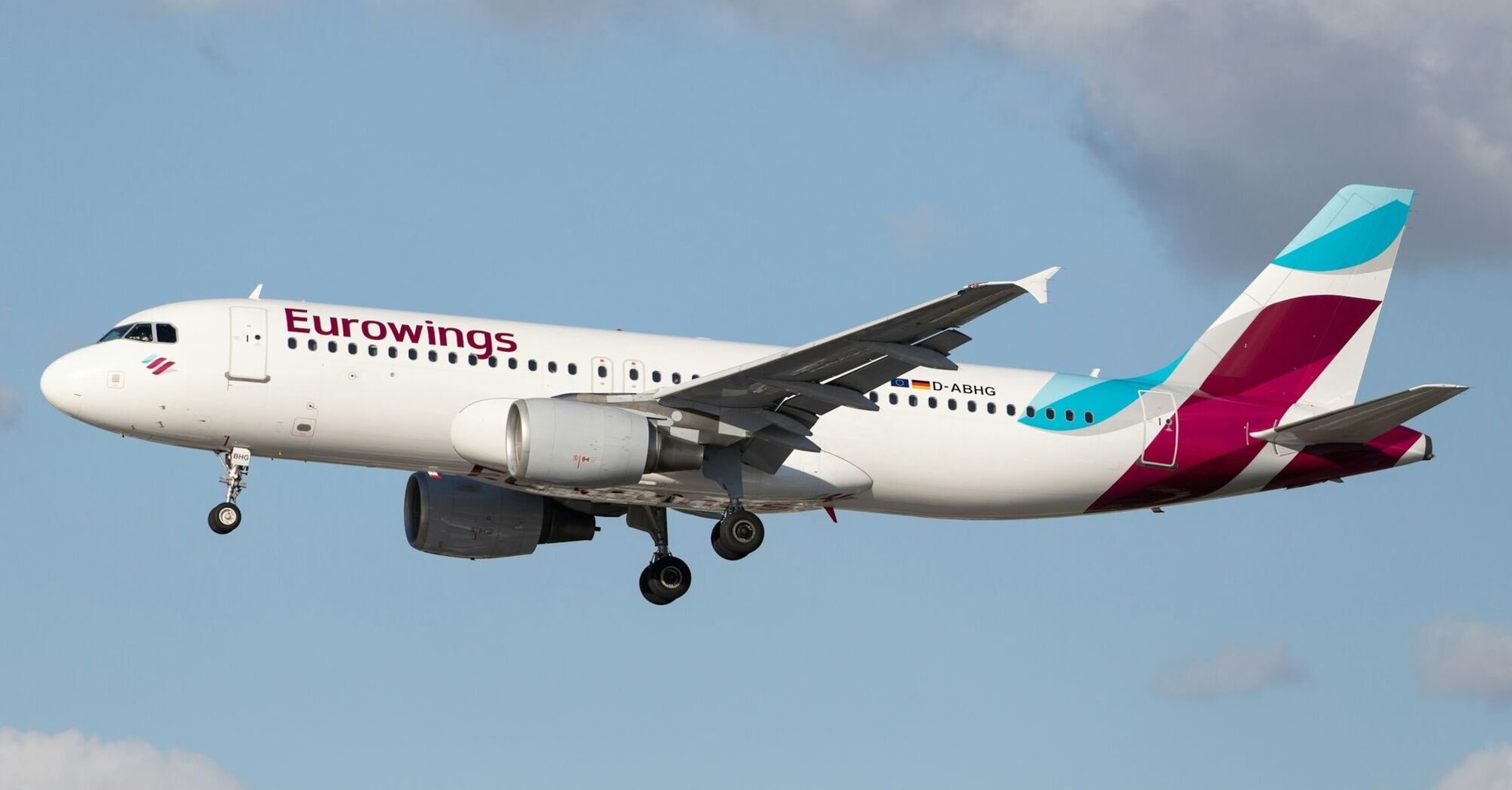 Eurowings plane landing with extended landing gear under a partly cloudy sky