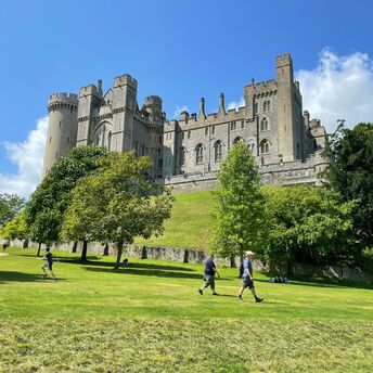 A view of Arundel Castle in West Sussex, surrounded by green lawns and trees, with visitors walking and enjoying the sunny day