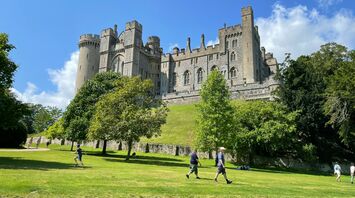 A view of Arundel Castle in West Sussex, surrounded by green lawns and trees, with visitors walking and enjoying the sunny day