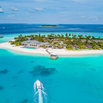 Aerial view of a tropical island resort in the Maldives with a speedboat approaching the shore