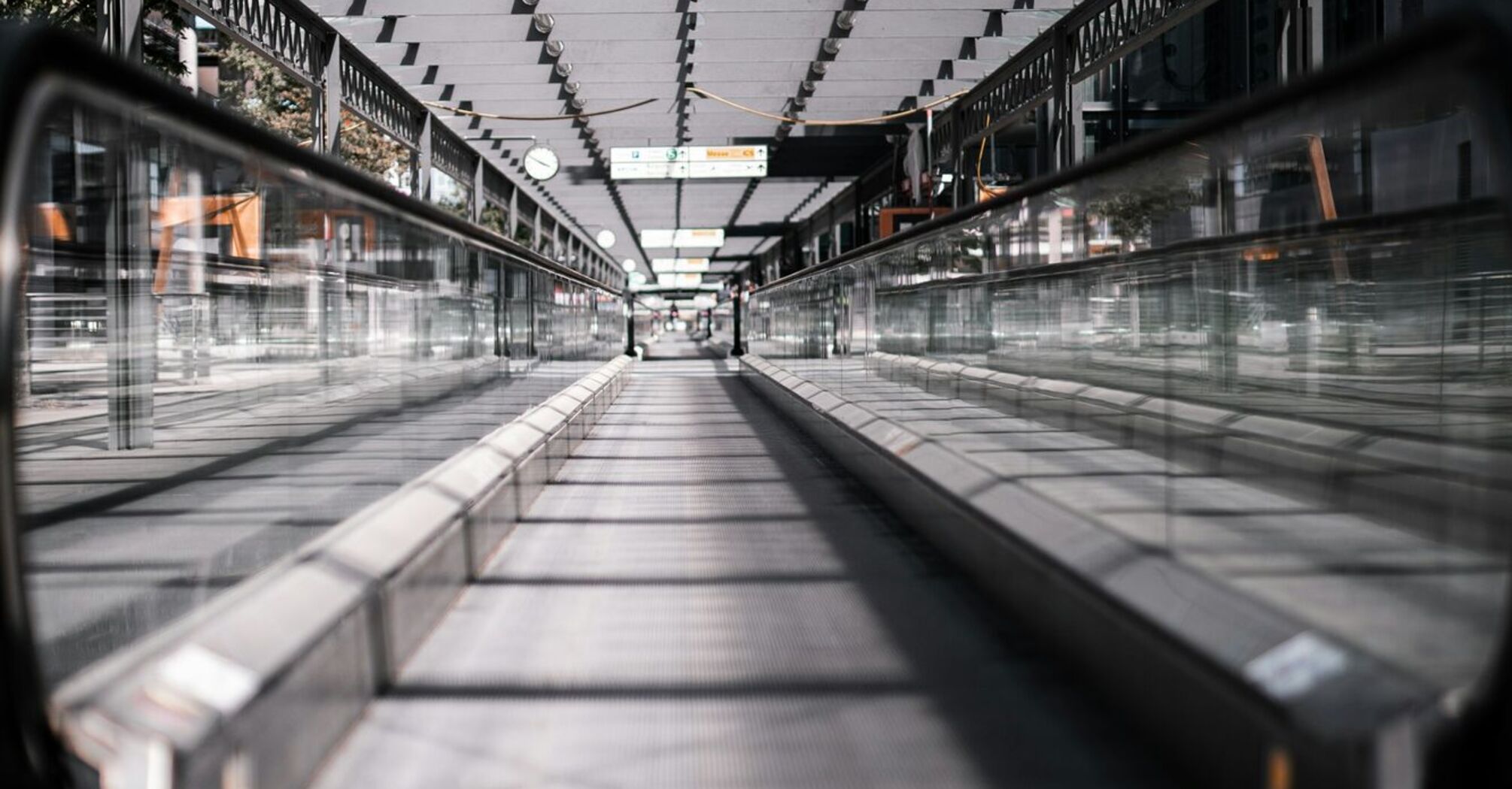 A modern moving walkway at an airport, covered with a glass roof and surrounded by sleek metal railings