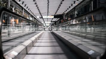 A modern moving walkway at an airport, covered with a glass roof and surrounded by sleek metal railings