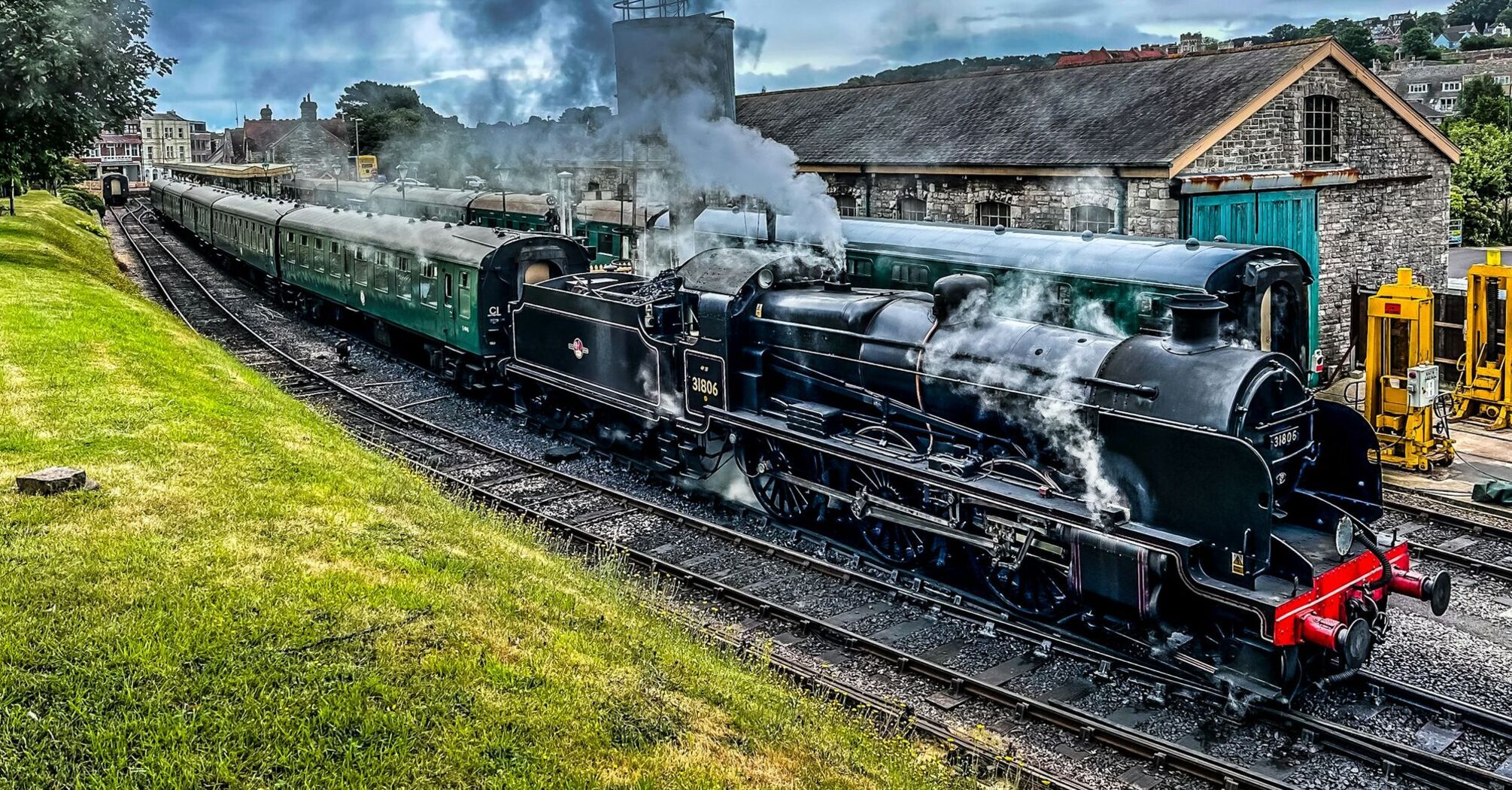 A vintage steam locomotive emitting smoke while pulling historic green passenger carriages at Swanage Railway