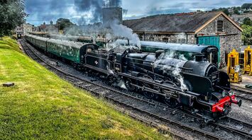A vintage steam locomotive emitting smoke while pulling historic green passenger carriages at Swanage Railway