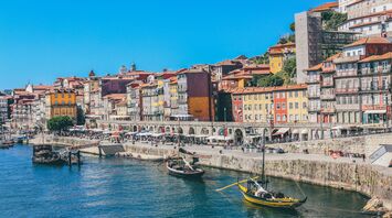 Colorful historic buildings line the waterfront of Porto, Portugal, with traditional boats floating on the Douro River under a bright blue sky