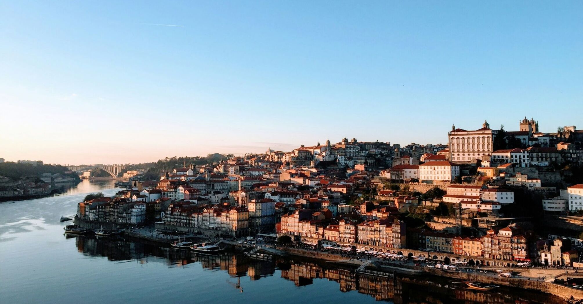 A panoramic view of Porto, Portugal, with the Douro River reflecting the city's historic architecture under a clear sky