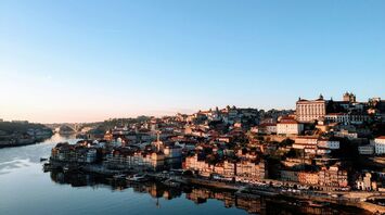 A panoramic view of Porto, Portugal, with the Douro River reflecting the city's historic architecture under a clear sky