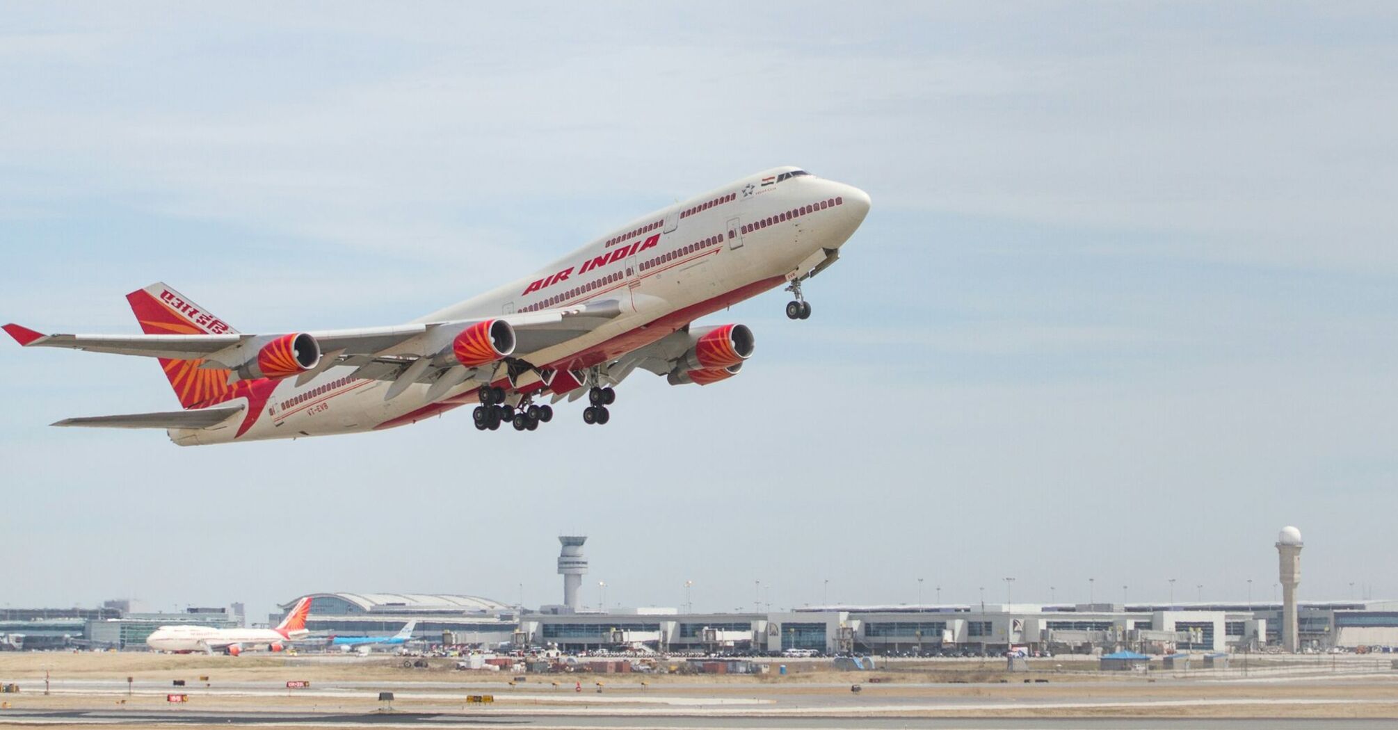 Air India aircraft taking off from an airport, with terminal buildings in the background